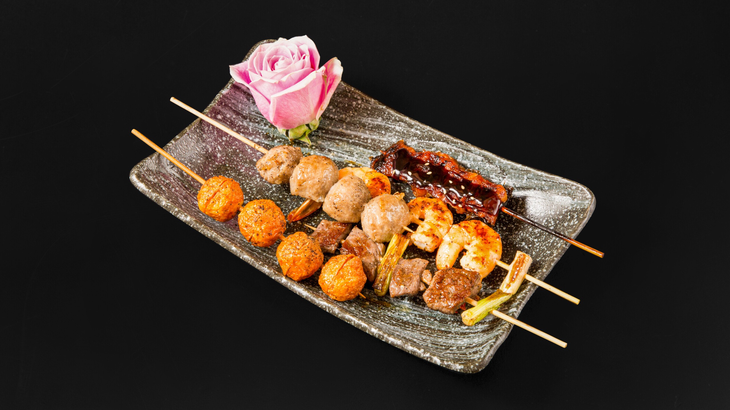 Assorted yakitori skewers including meatballs, shrimp, beef with a pink rose garnish at Wafuu Izakaya, a Japanese Restaurant in Forest Hills