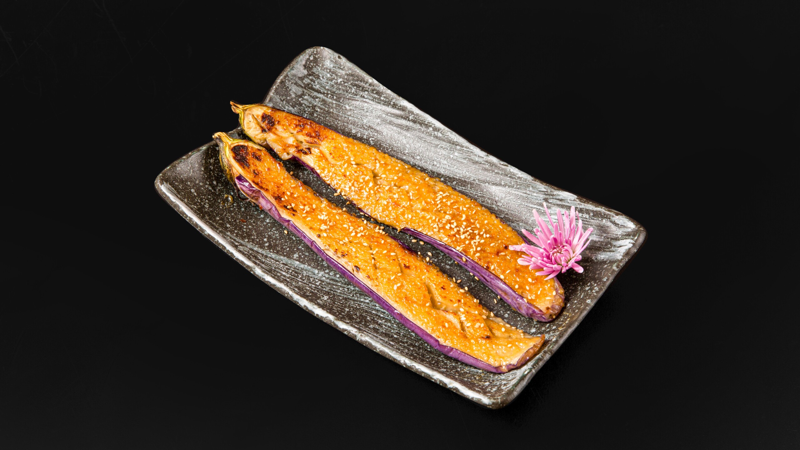 Grilled eggplant with sesame seeds and a pink flower garnish at Wafuu Izakaya, a Japanese Restaurant in Forest Hills