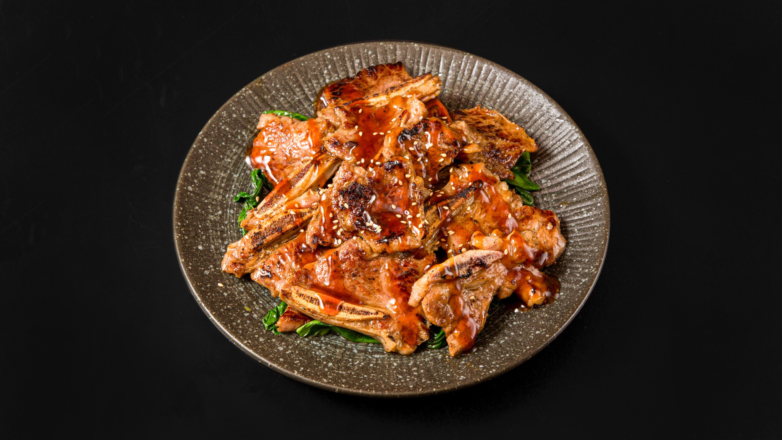 Grilled pork ribs with sauce and sesame seeds on a plate at Wafuu Izakaya, a Japanese Restaurant in Forest Hills