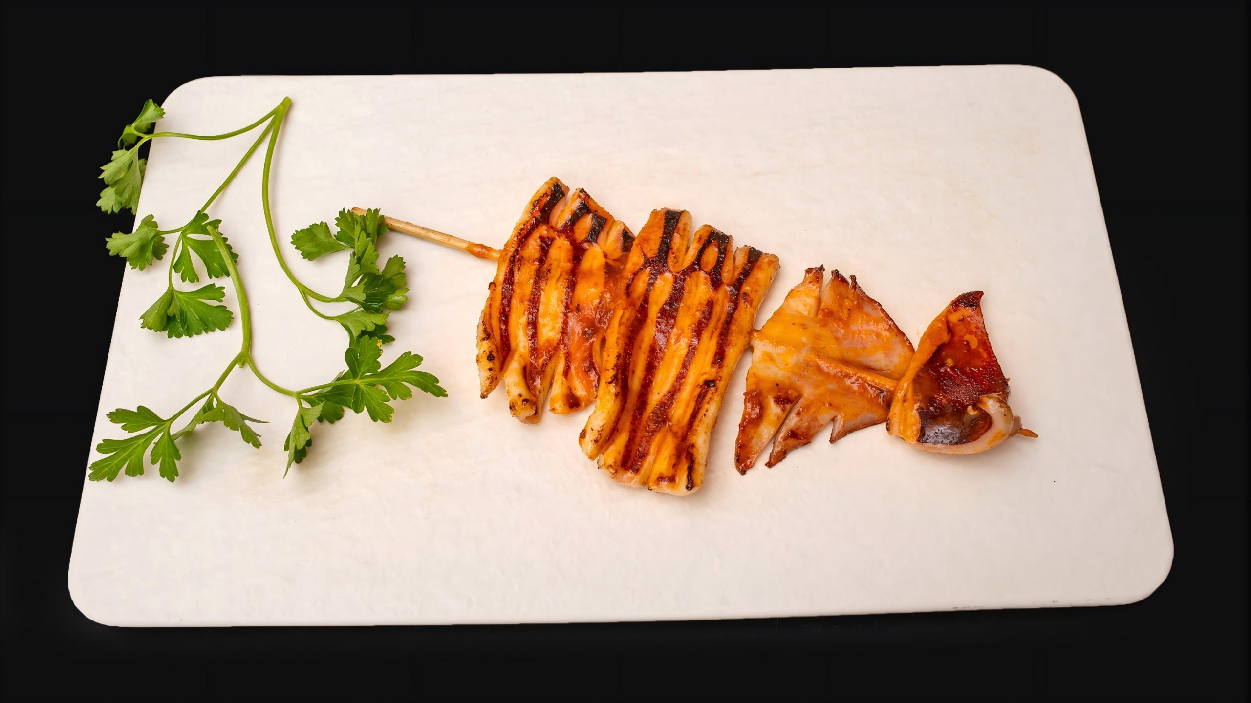 Grilled squid skewer with parsley on a white board at Wafuu Izakaya, a Japanese Restaurant in Forest Hills